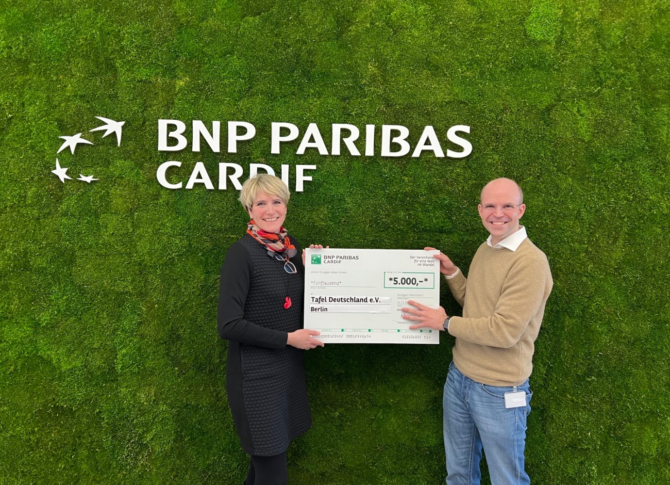 Nicolas Pöltl und Andrea Geiling stehen vor Wand mit BNP Paribas Cardif Logo und halten den Spendenschein