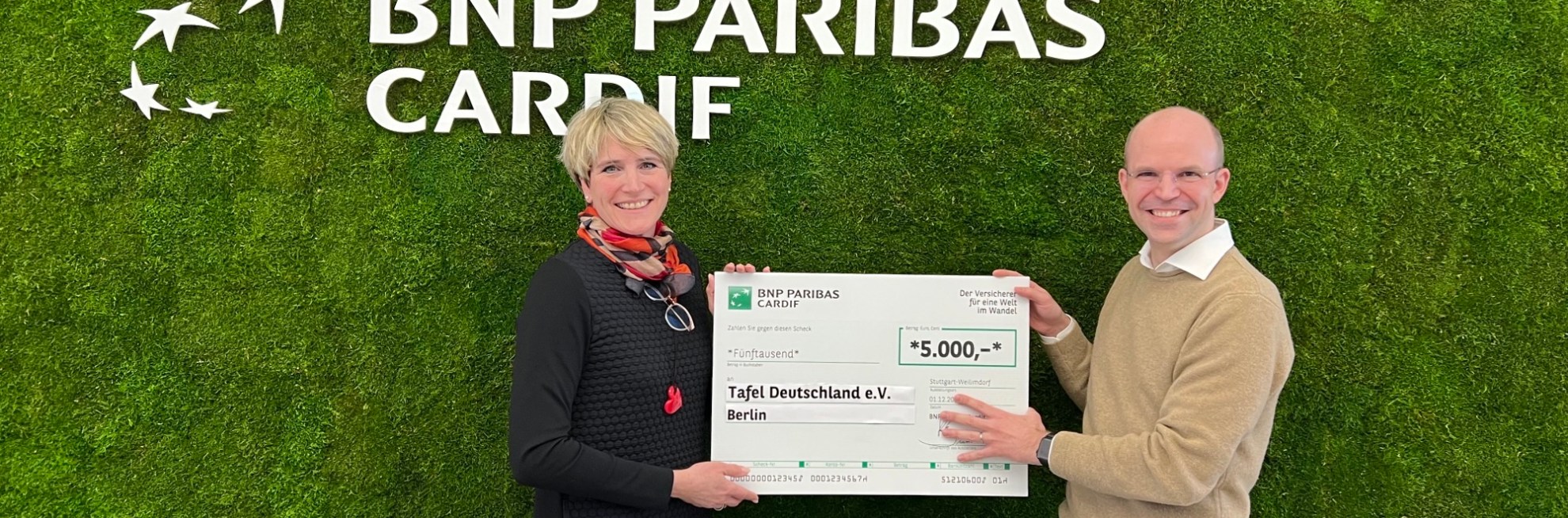 Nicolas Pöltl und Andrea Geiling stehen vor Wand mit BNP Paribas Cardif Logo und halten den Spendenschein