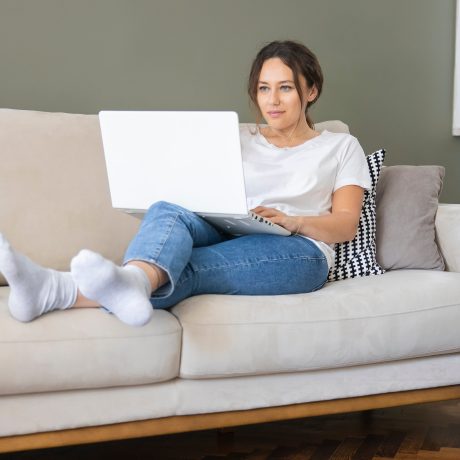 Frau liegt auf dem Sofa mit Laptop auf dem Schoß
