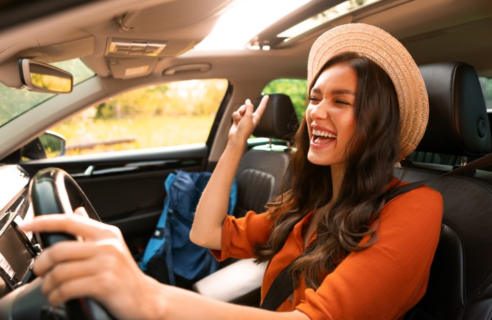 Frau fährt alleine Auto, singt und tanzt zu Musik